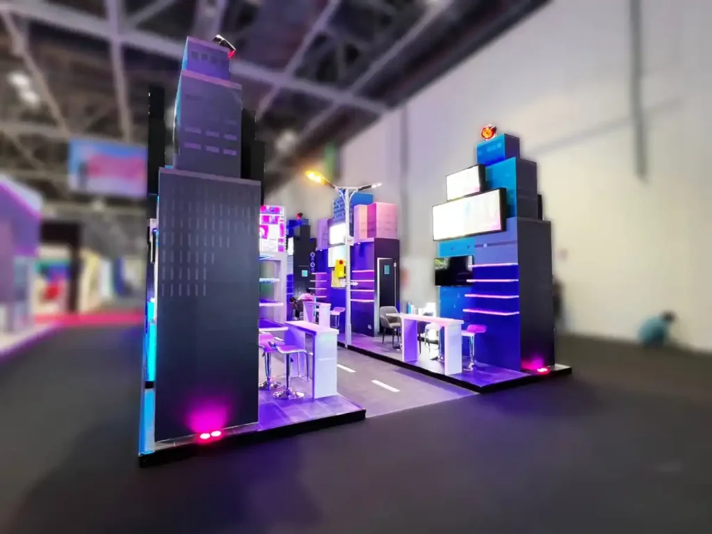 Modern trade show booth designed like a futuristic city with illuminated towers, display shelves, and meeting counters