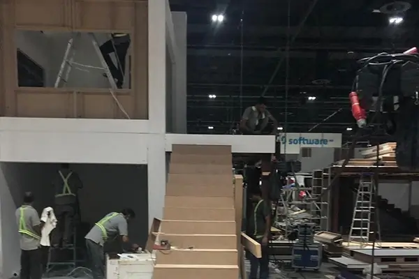 Exhibition booth construction showing staircase installation, structural assembly, and onsite build progress