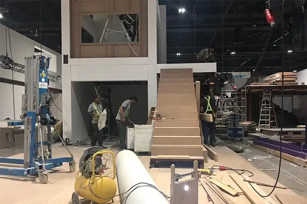 Exhibition booth under construction with staircase, structural framing, and installation team preparing upper level