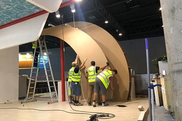 Exhibition stand installation team assembling curved structural elements during custom booth construction