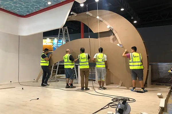 Exhibition booth construction in progress with installers positioning curved framework for custom stand build