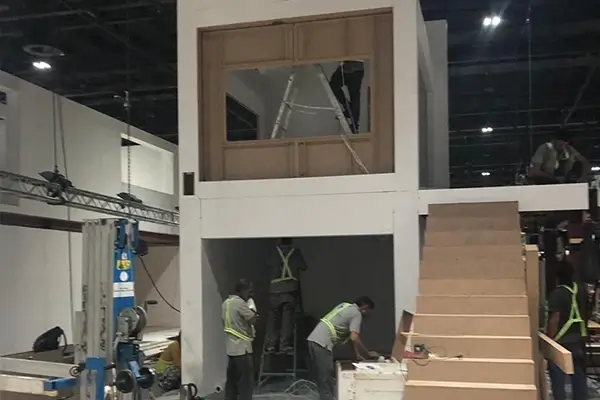 Exhibition stand interior construction with installers working on partitions, staircase, and structural framework