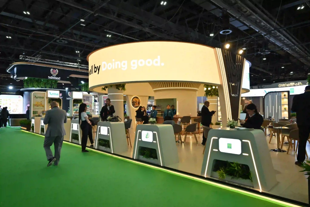 Modern trade show booth featuring illuminated counters, lounge seating, and overhead signage