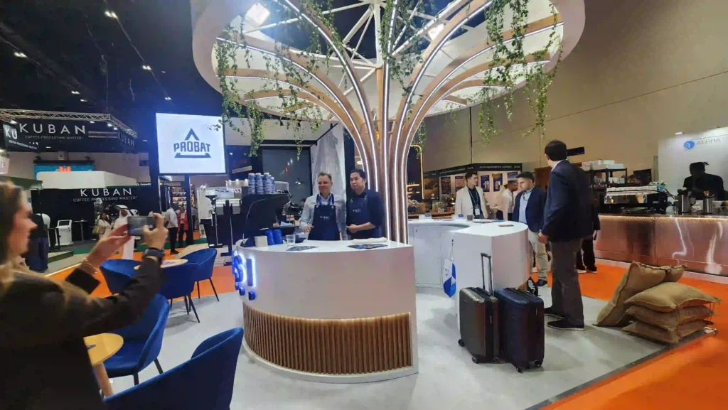 Custom exhibition stand with curved counters, decorative canopy, seating, and hanging greenery