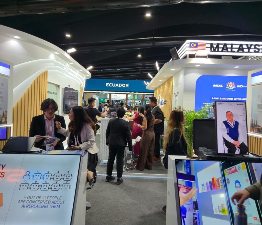 Busy Malaysia Digital trade show booth featuring interactive screens and branded displays