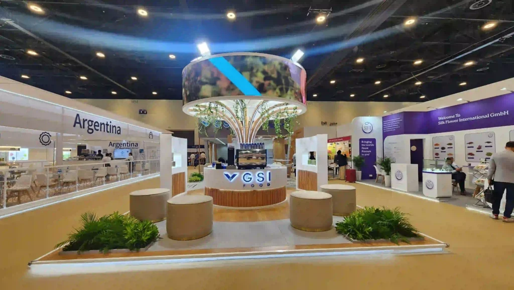Modern custom exhibition stand featuring central reception, circular canopy, seating, and greenery
