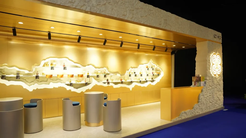 Gold exhibition stand interior with illuminated product shelves, round tables, and contemporary chairs.
