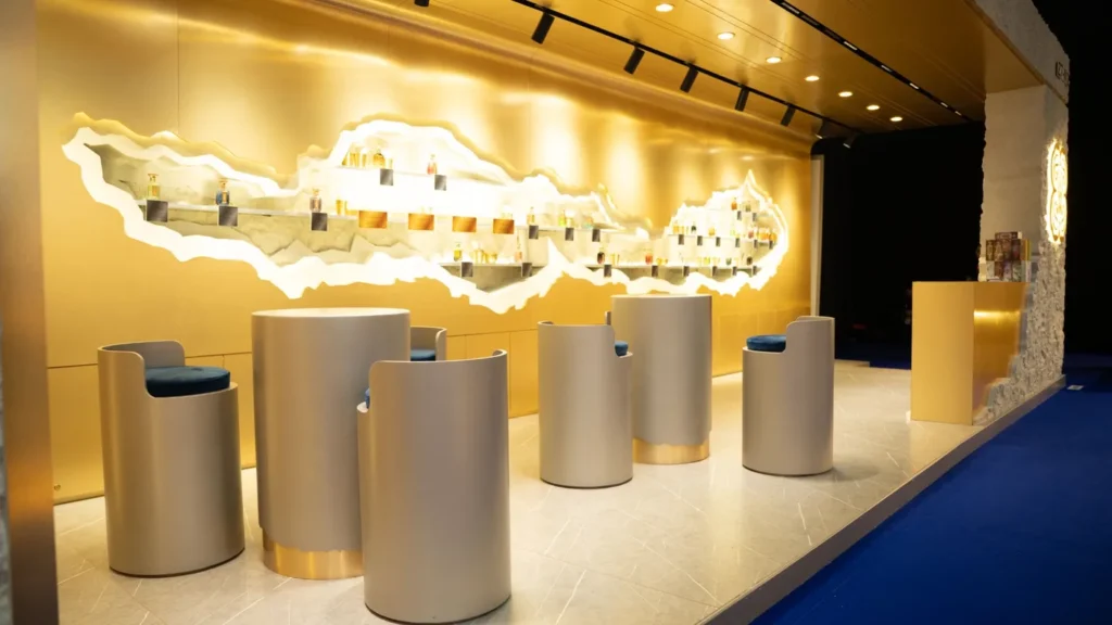 Gold exhibition stand featuring a reception counter, illuminated branding, and modern product shelving.