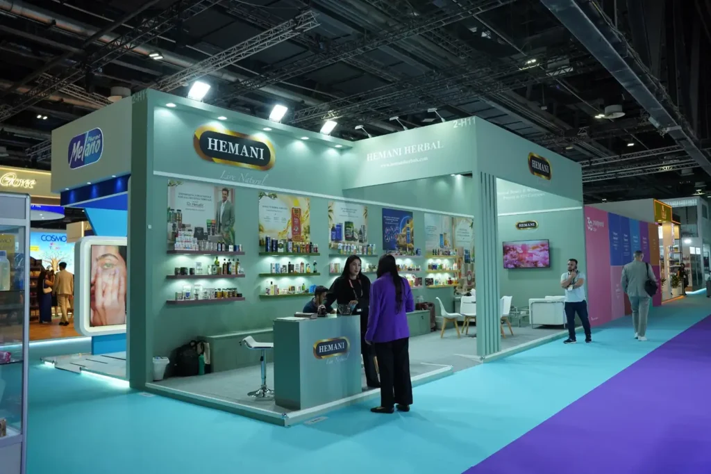 Hemani exhibition booth with illuminated branding, herbal product displays, and white seating