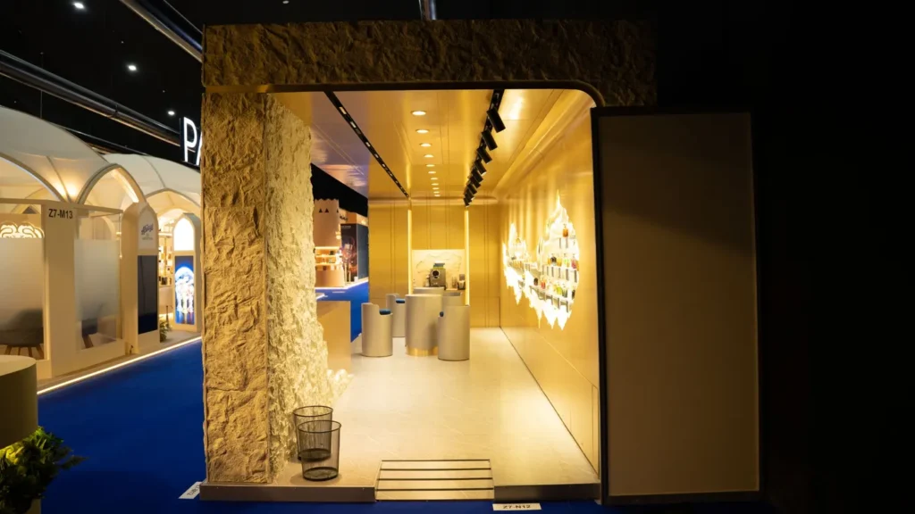 Luxury exhibition stand with illuminated display shelves, gold wall panels, and contemporary furniture.