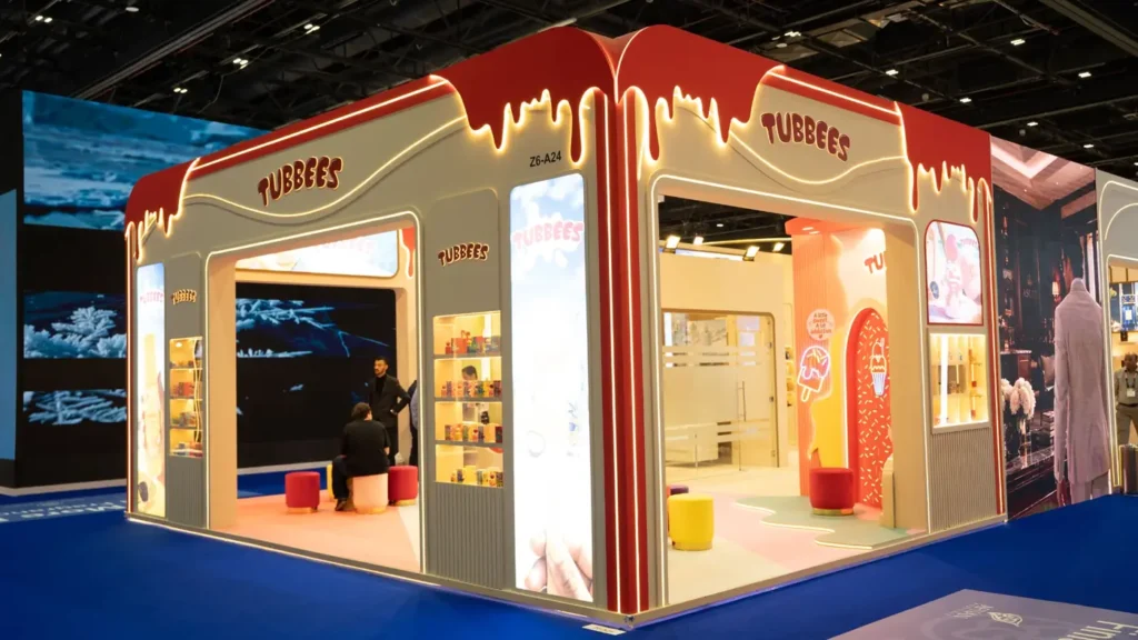 Tubbees trade show booth with curved illuminated signage, product displays, and blue exhibition flooring.